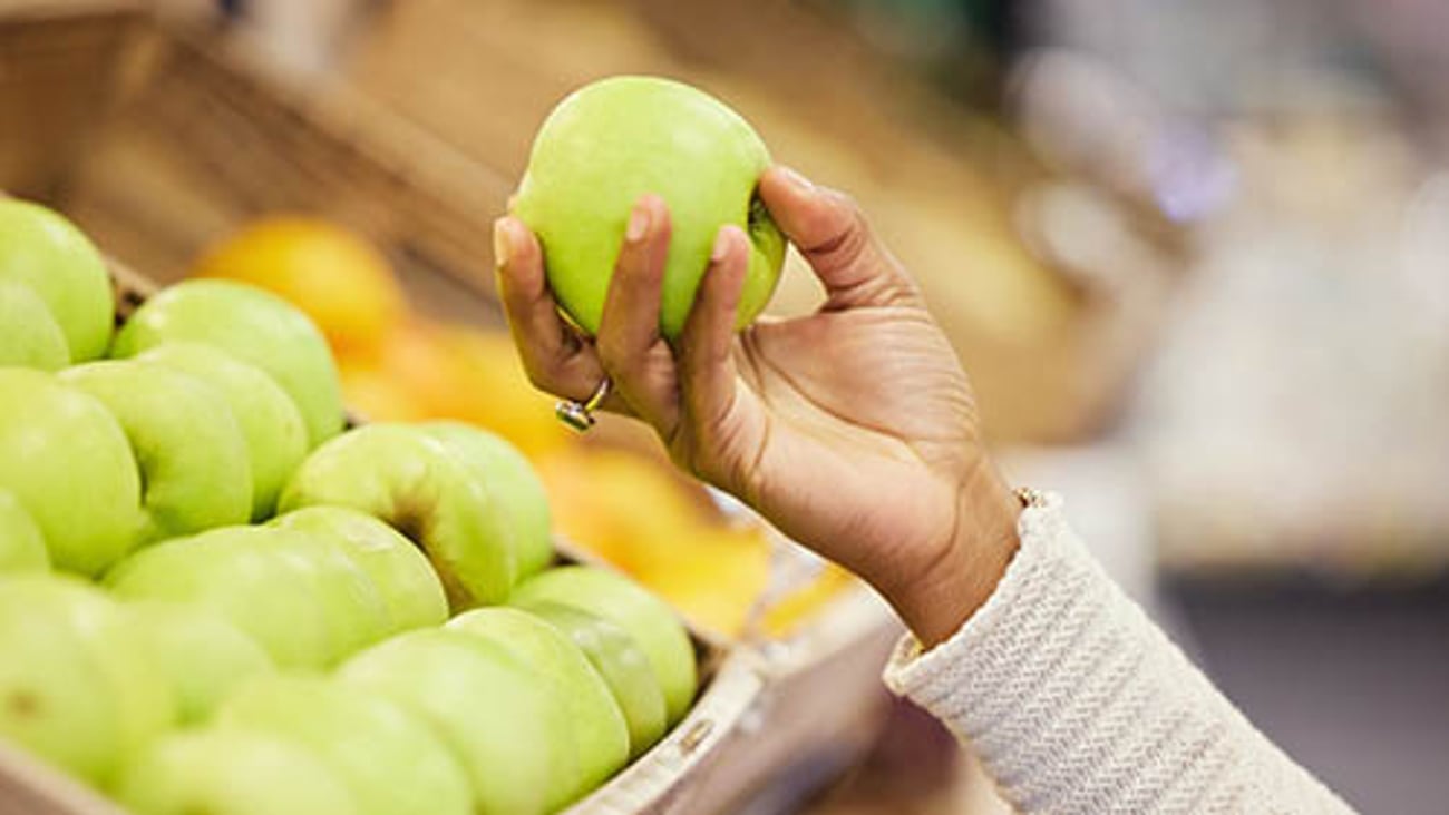 Woman's Hand Holding Apple in Grocery Store Teaser