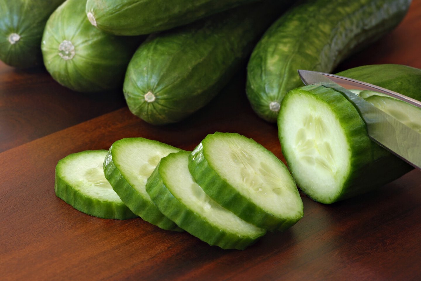 Freshly sliced mini cucumbers with knife on wooden cutting board.  Macro with shallow dof.  Focus on front slices.; Shutterstock ID 71318215