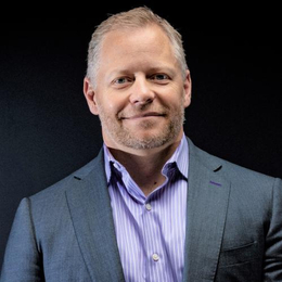 a man wearing a suit and tie smiling at the camera